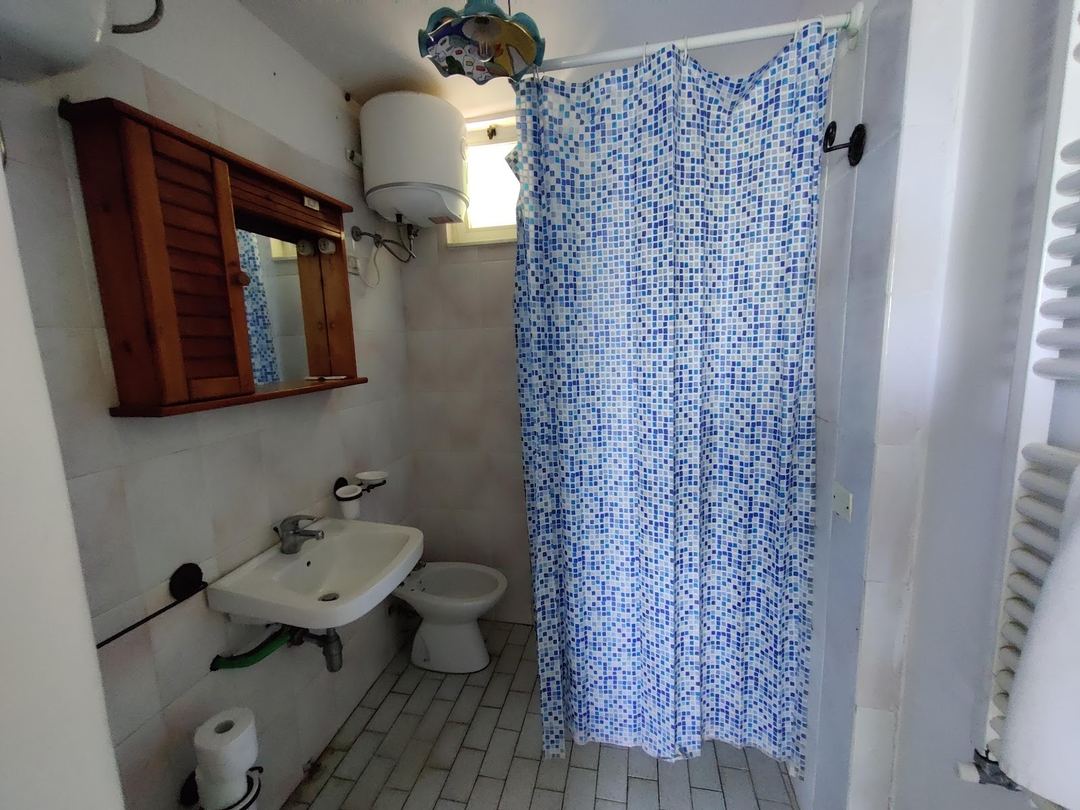 A bathroom with a sink, toilet, shower with blue mosaic tile curtain, and wall-mounted mirror.