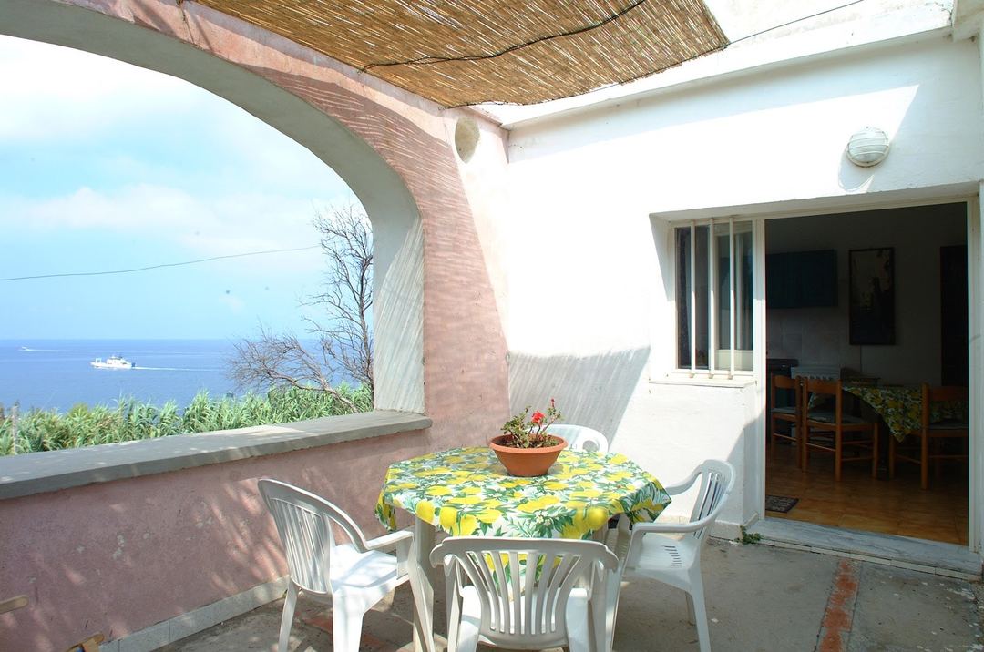 A seaside terrace with a yellow floral tablecloth overlooking the Mediterranean Sea with a cruise ship visible on the horizon.