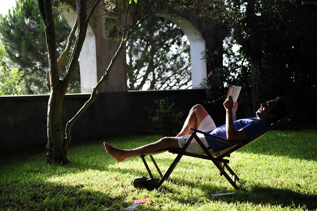 A guest relaxes in a lounge chair while reading in the shaded garden area of the property.